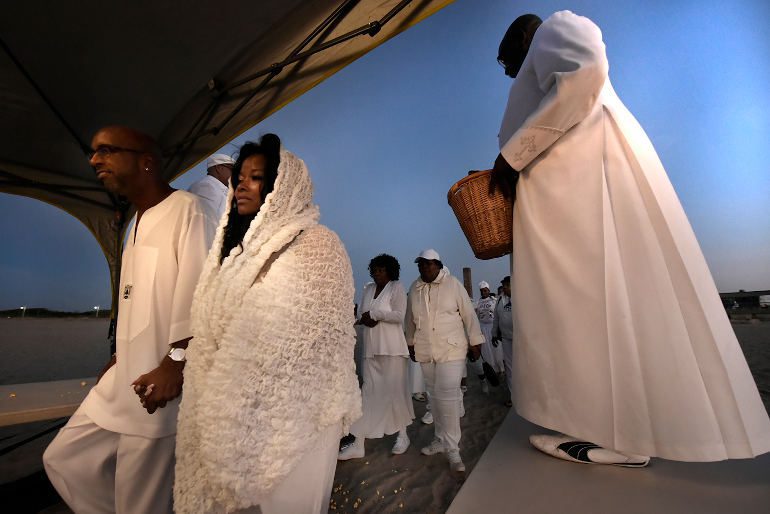 In this image people are walking in twos to be blessed – the ritual involves dropping popcorn on the heads as one walks through a canvas tent which symbolizes the door of no return which according to pastor Richard Honeywell was a ritual originating in Brazil and symbolizes healing for the body and mind. MAAFA ceremony in Far Rockaway at Reese beach organized by the St Paul's Community Baptist Church, Brooklyn NYC