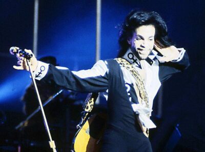 image of Prince Rogers Nelson holding microphone blue background while on stage